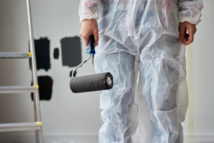Une femme peint un mur intérieur avec un rouleau, appliquant une peinture bleue sur une surface blanche