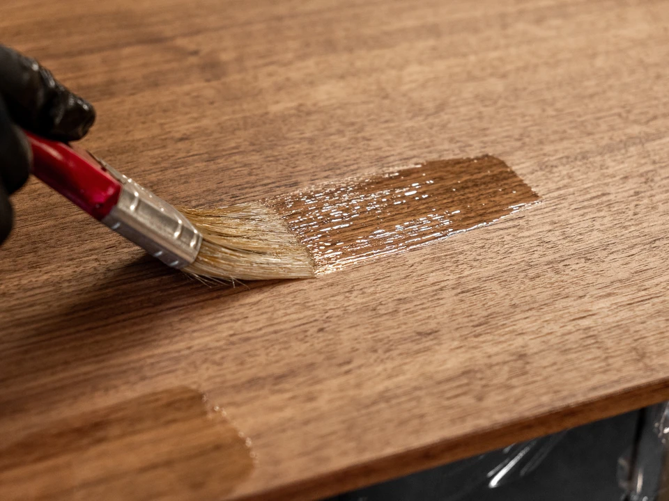 Intérieur d'atelier, personne portant gants blancs appliquant peinture au pinceau sur meuble en bois clair